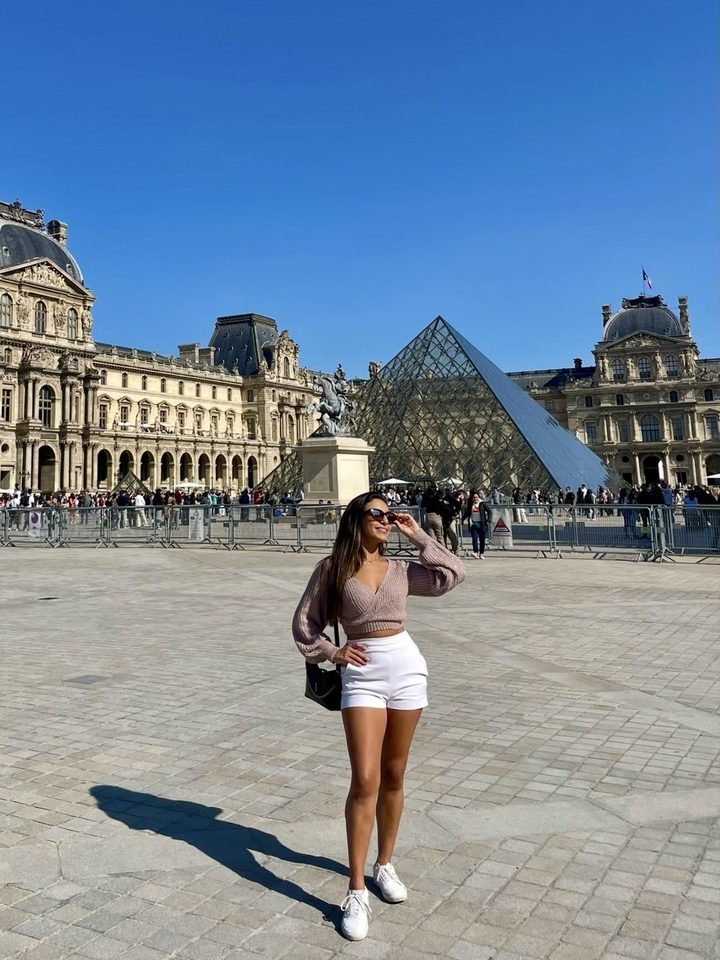 Natasha em uma praça, com uma pirâmide de vidro e um palácio ao fundo
